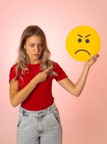 woman pointing at cut out of sad face emoji